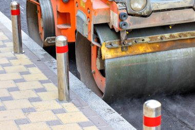 Titreşen bir patenin metal silindiri, güneşli bir günde yolda taze asfaltı sıkıştırır. Yakın plan. Boşluğu kopyala.