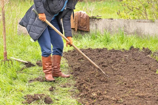 一位穿着黑色夹克的中年妇女在个人土地上用金属耙松动地面 — 图库照片