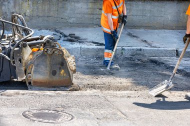 Yol işçileri eski asfaltı menteşeli bir endüstriyel kesiciyle temizleyip yol yüzeyini küreklerle temizliyorlar..