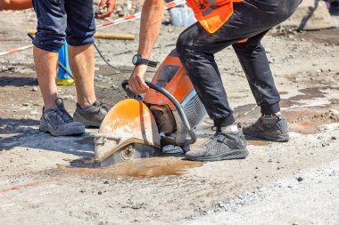 Bir işçinin elindeki benzin dairesel kesicisi güneşli bir yaz gününde asfalt c oncrete yol yüzeyini keser. Boşluğu kopyala.