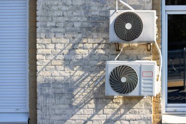 External air conditioner units on an old brick wall with a fragment of a metal-plastic window and metal blinds.
