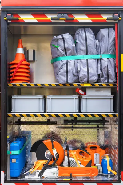 Stock image The cargo compartment of a loaded fire truck contains a chainsaw, rotary cutter, traffic cones, fire suits and plastic tool boxes.