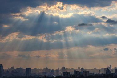 Şafak ışınları, uyuyan bir şehirdeki evlerin siluetlerinin üzerindeki kalın bulutları delip geçer. Dramatik bir sabah gökyüzünde parlak bir ışık.