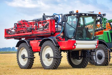 Modern bir püskürtme makinesi, verimli ürün koruması için donanımlı altın tarlalarda gururla durur. Açık gökyüzü makinelerin canlı renklerini artırıyor, tarımsal yenilikler sergiliyor..