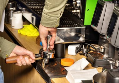 In a bustling coffee shop, a skilled barista expertly tamps coffee grounds into a portafilter, preparing for the perfect espresso shot. The atmosphere buzzes with energy and aroma. clipart