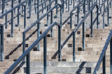 Metal korkuluklarla çevrili sağlam beton basamaklar sistematik olarak yükseliyor. Gölgeler karmaşık desenler sergilerken canlı dokular bu mimari mucizeye hayat veriyor..