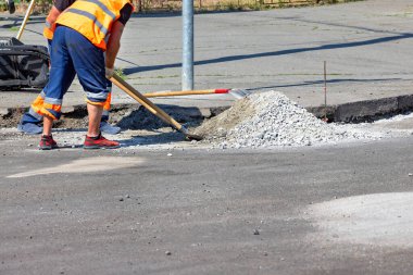 Sıcak güneşin altında, canlı teçhizatlı çalışkan bir inşaat işçisi çakıllarla çalışmak için bir kürek kullanarak yol onarımı yapıyor. Boşluğu kopyala.