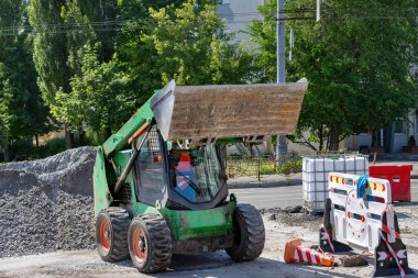 Yeşil bir fren dümeni, gün ortası güneşinin altında çakıl ve inşaat malzemeleriyle çevrili hareketli bir inşaat sahasında manevra yapıyor..