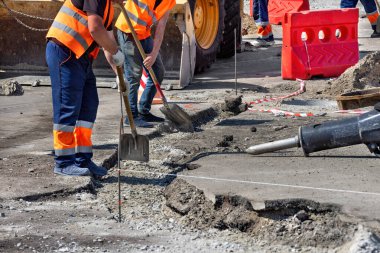 İşçiler inşaat ekipmanları ve güvenlik bariyerleriyle çevrili kentsel bir bölgedeki kaldırımları özenle onarıyorlar.
