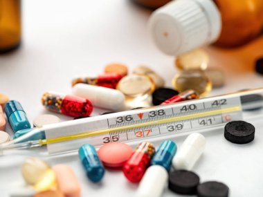 Renkli kapsüller, tabletler ve bir yüzeye yerleştirilmiş cıva termometresi önemli sağlık göstergelerini vurguluyor. Sahne, tıbbi bakım ve kişisel sağlığa odaklanmış bir anı yakalıyor..