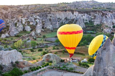 Renkli sıcak hava balonları, Cappadocia 'nın büyüleyici manzarasının üstündeki gökyüzüne çıkar. Peri bacaları ve yemyeşil bitkilerle doludur..