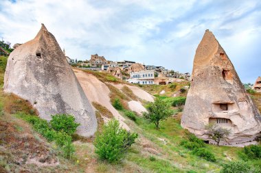 Cappadocia 'nın gerçeküstü peri bacaları alacakaranlık gökyüzüne karşı kule, antik mağara evleri yeşil yamaçlar arasında yerleşmiş.