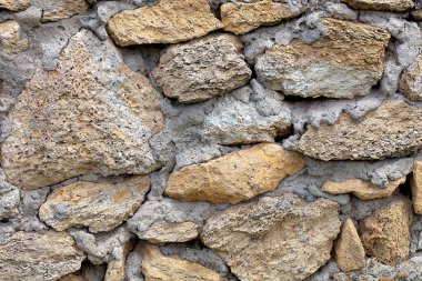 Kırsal taştan bir duvarın yakın plan görüntüsü, sert doğal taşların gri havan topu ile dikkatlice düzenlendiği yer. Topraksı dokular ve renkler sıcak ve kalıcı bir atmosfer yaratır..