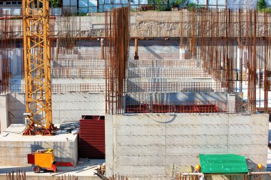 İşçiler, çelik inşaat demirleri ve beton formlarla çevrili yoğun bir inşaat alanında işbirliği yapıyorlar. Bir vinç dimdik dururken, makineler bu kentsel manzaranın geleceğini şekillendirmeye yardımcı oluyor..
