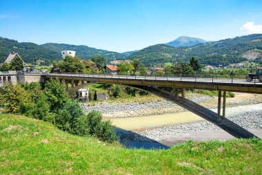 Resimli bir köprü yeşil yeşil ve görkemli dağlarla çevrili sakin bir nehri kapsar. Güneş ışıl ışıl parlıyor. Huzurlu manzaraya ve davetkar keşiflere sıcak bir parıltı saçıyor..