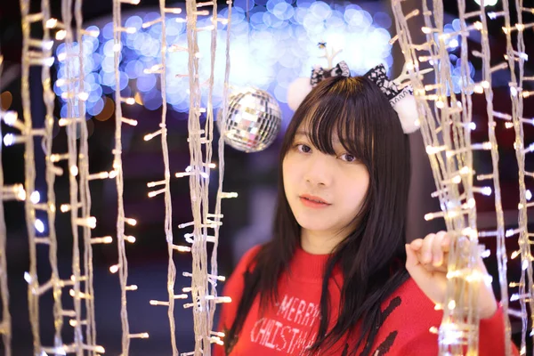 美丽的亚洲年轻女子 穿着红色毛衣 圣诞树灯火通明 — 图库照片