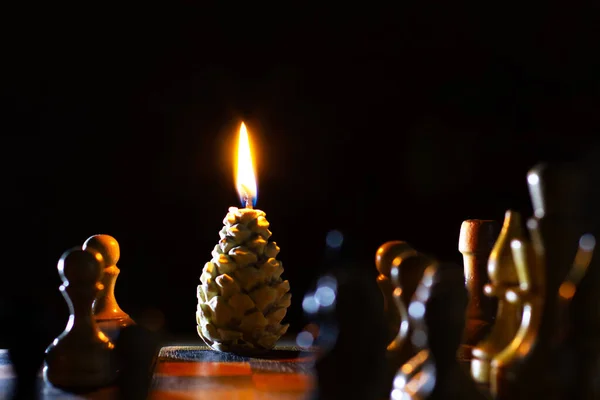 松の円錐形のキャンドルを燃焼 前景のチェス 手作りだ 休日の到来 暗い背景のろうそく — ストック写真