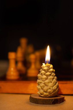 Çam kozalağı şeklinde yanan mum. Satranç arka planda. El yapımı. Tatil Gelişi