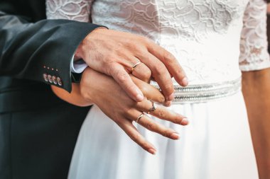 Gelin ve damadın evlilik yüzükleriyle süslenmiş ellerinin yakın plan fotoğrafı. Birbirlerine dolanmış parmaklarının güzelliği. Gelin ve damadın elinde yüzükler