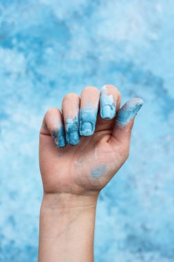 Mavi arka planda boyalı güzel bir kadın eli. Boyalı parmaklar. Yakın plan.