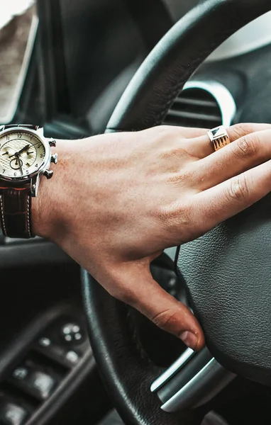 A man holds the steering wheel of a luxury car. Watch and a ring on his hand