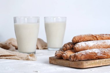 Fotografas de horchata de chufa servida en vasos de cristal, acompaada de fartones sobre una tabla de madera. Composicin minimalista con fondo blanco, ideal para ilustrar la gastronoma valenciana,