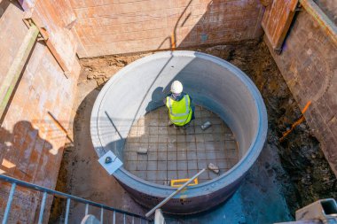 Groundworker working in new built deep manhole during drainage works marking for pipes position