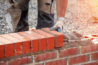 Industrial bricklayer laying bricks on cement mix on construction site