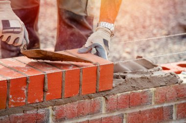 Industrial bricklayer laying bricks on cement mix on construction site