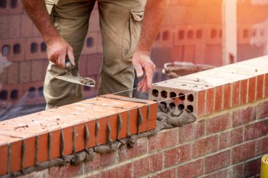 Industrial bricklayer laying bricks on cement mix on construction site