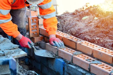 Industrial bricklayer laying bricks on cement mix on construction site. Fighting housing crisis by building more affordable houses concept