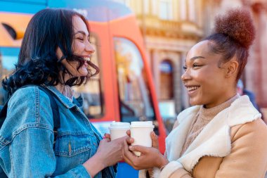 two women in a denim jacket is talking to each other , drinking coffee  and waiting for a tram at the stop Lifestyle photo