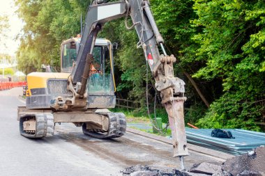Excavator with hydraulic jack hammer  breaking asphalt in preparation for drainage works close up and selective focus