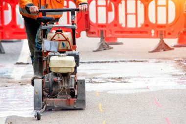 İnşaatçı, asfalt yol yüzeyini kesmek için demir testeresi kullanıyor.