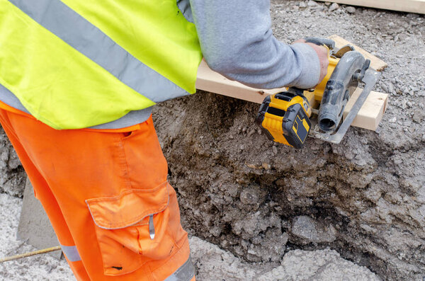 Строитель резки древесины с беспроводной батарейной циркулярной пилой на строительной площадке