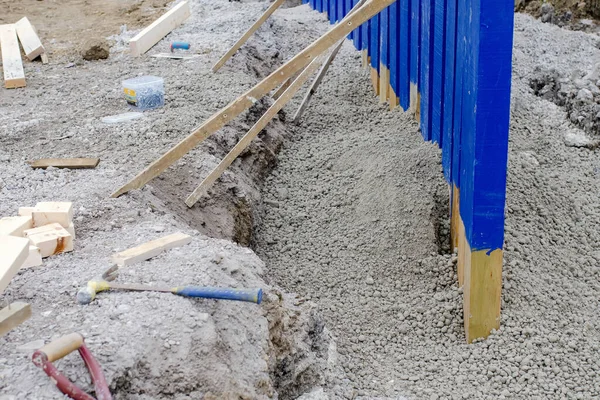 Builder installing rail slippers painted blue into semi-dry concrete to form a secure barrier around new school playground as part of extra safety measures