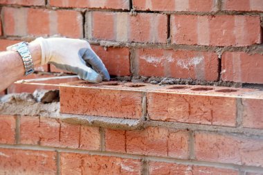 Close up of industrial bricklayer laying bricks on cement mix on construction site