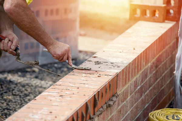 Close up of a brick wall and jointer trowel used by the worker to apply and level the mortar between bricks. Bricklayer making finishing touches to the brick wall and filling joints with mortar