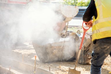 Excavator bucket filled with concrete to pour concrete into formwork on building site