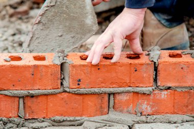 Close up of industrial bricklayer laying bricks on cement mix on construction site
