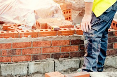 Close up of industrial bricklayer laying bricks on cement mix on construction site