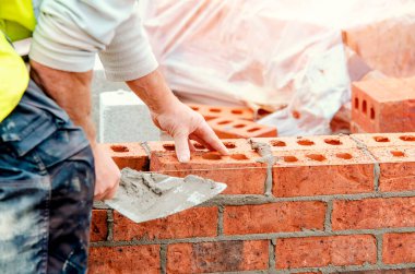 Close up of industrial bricklayer laying bricks on cement mix on construction site