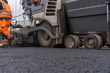 Sıcak asfalt kaldırım taşı yeni yerleşim alanı üzerine yeni yol yüzeyi döşeyen ve yanında turuncu hi-viz 'deki yol işçisi operatörü