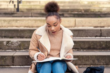Afrika kökenli kadın öğrenci bir not defterine yazıyor, şehirdeki merdivenlere plan yapıyor. Sıkı çalışma konsepti Yaşam tarzı fotoğrafı
