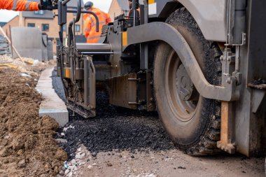 Sıcak asfalt kaldırım taşı yeni yerleşim alanı üzerine yeni yol yüzeyi döşeyen ve yanında turuncu hi-viz 'deki yol işçisi operatörü