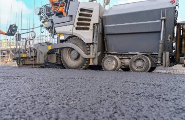 Sıcak asfalt kaldırım taşı yeni yerleşim alanı üzerine yeni yol yüzeyi döşeyen ve yanında turuncu hi-viz 'deki yol işçisi operatörü