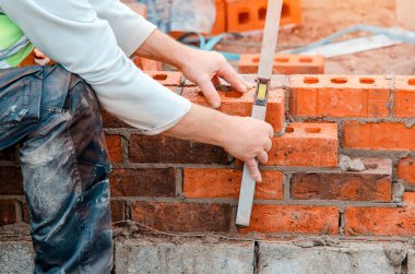 Hard working bricklayer lays bricks on cement mix on construction site. Fight housing crisis by building more affordable houses concept