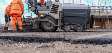 Sıcak asfalt kaldırım taşı yeni yerleşim alanı üzerine yeni yol yüzeyi döşeyen ve yanında turuncu hi-viz 'deki yol işçisi operatörü