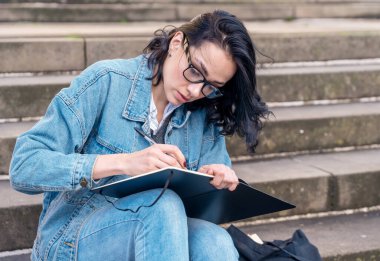Not defterine yazı yazan kadın öğrenci, şehir konsepti olan 