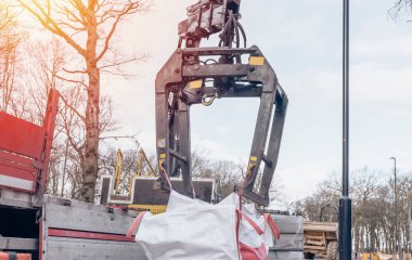 Dropside plakalı HIAB vinç kamyonu tuğla kapma eklentisiyle inşaat alanına malzeme getiriyor ve indiriyor.